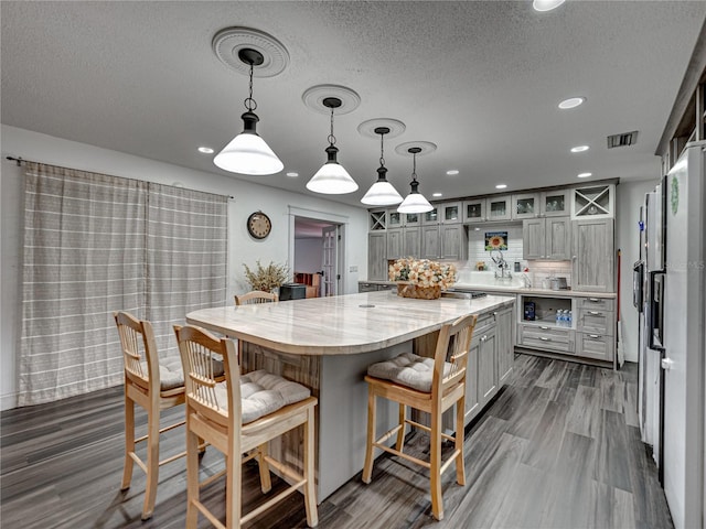 kitchen with a kitchen bar, decorative light fixtures, a kitchen island, decorative backsplash, and dark wood-type flooring