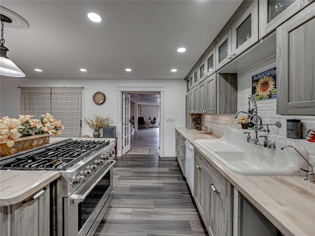 kitchen with stainless steel stove, sink, pendant lighting, backsplash, and dark wood-type flooring