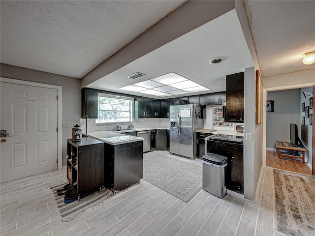 kitchen featuring light hardwood / wood-style flooring, a textured ceiling, kitchen peninsula, appliances with stainless steel finishes, and sink