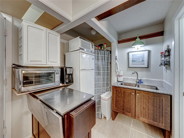 kitchen with white fridge, light tile patterned flooring, white cabinets, sink, and a textured ceiling