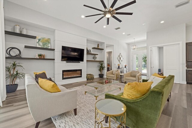 living room with french doors, wood-type flooring, ceiling fan, and a large fireplace