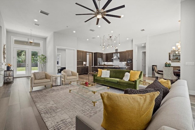 living room with french doors, ceiling fan with notable chandelier, and light hardwood / wood-style flooring