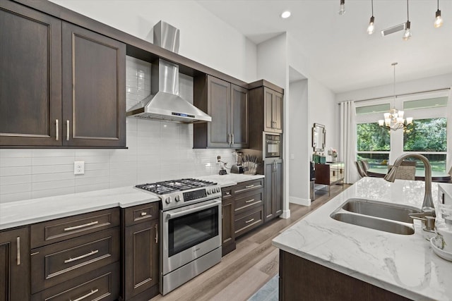 kitchen with light stone countertops, a notable chandelier, sink, wall chimney exhaust hood, and stainless steel gas range oven