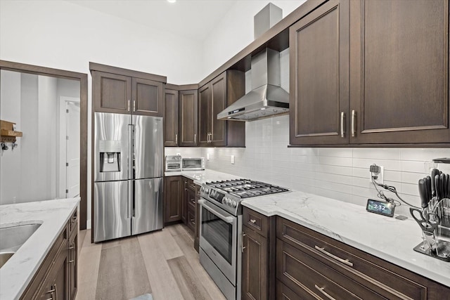 kitchen with light hardwood / wood-style flooring, stainless steel appliances, light stone countertops, decorative backsplash, and wall chimney exhaust hood