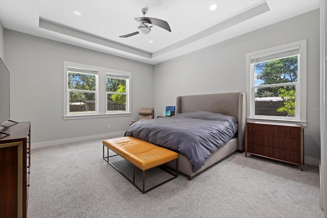 bedroom with ceiling fan, a raised ceiling, and light carpet