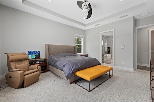 bedroom featuring ceiling fan, light colored carpet, a raised ceiling, and ensuite bath