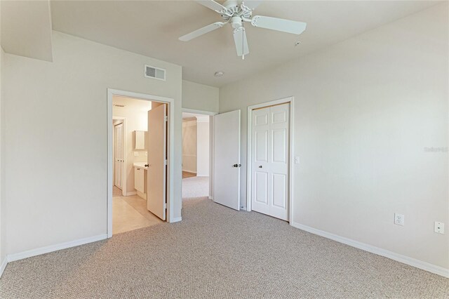 unfurnished bedroom with ceiling fan, ensuite bathroom, light carpet, and a closet