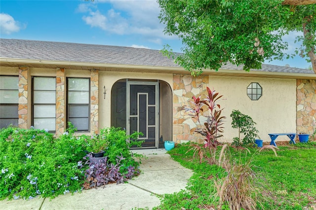 property entrance featuring stucco siding, stone siding, and a shingled roof