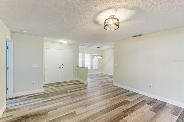 empty room with visible vents, a textured ceiling, light wood-type flooring, and baseboards