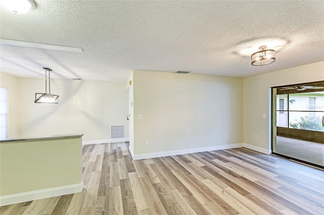 empty room featuring visible vents, baseboards, light wood-style floors, and a textured ceiling