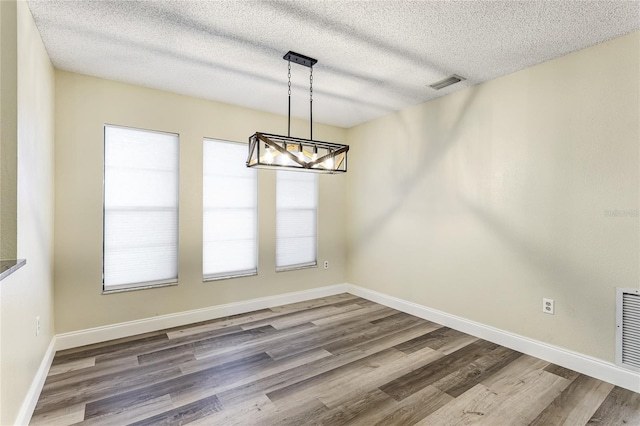 unfurnished dining area featuring a textured ceiling, a notable chandelier, and hardwood / wood-style floors