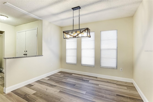 unfurnished dining area featuring light wood-type flooring, a wealth of natural light, and a textured ceiling