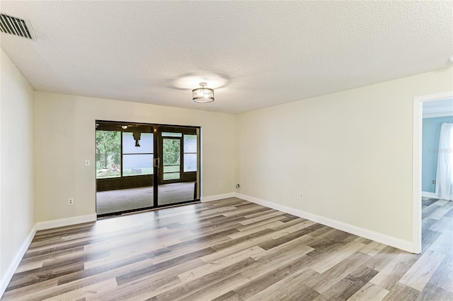 empty room with light wood finished floors, visible vents, a textured ceiling, and baseboards