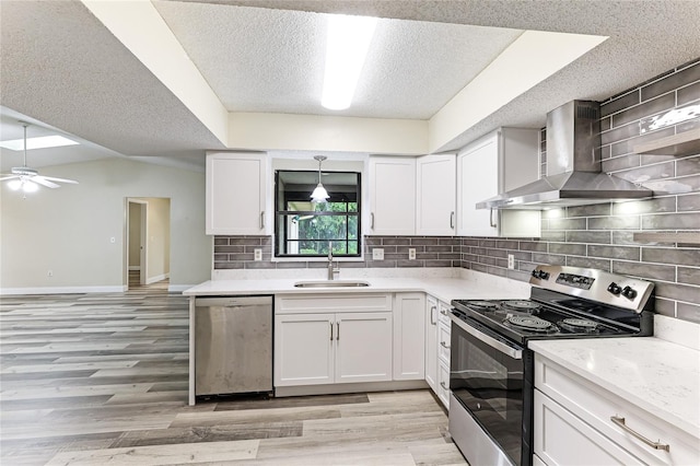 kitchen with ceiling fan, appliances with stainless steel finishes, white cabinets, and wall chimney exhaust hood