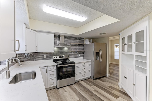 kitchen with wall chimney exhaust hood, appliances with stainless steel finishes, light hardwood / wood-style floors, sink, and white cabinets