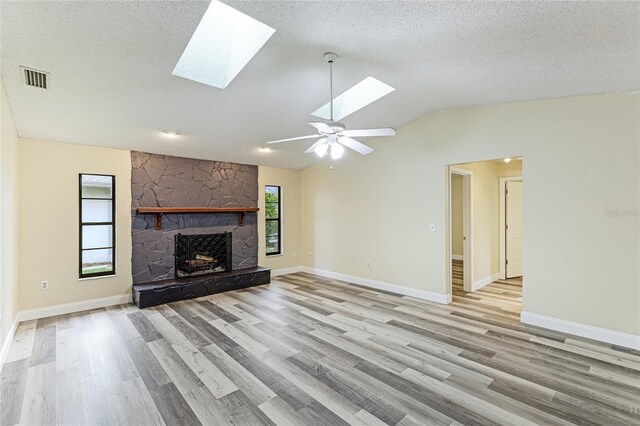 unfurnished living room with a fireplace, light hardwood / wood-style floors, vaulted ceiling with skylight, ceiling fan, and a textured ceiling