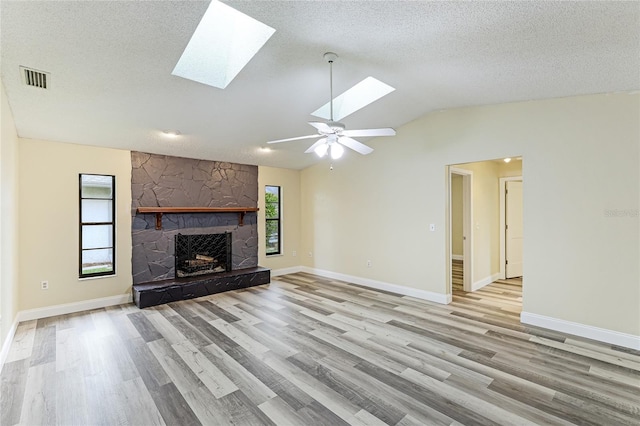 unfurnished living room with a stone fireplace, vaulted ceiling with skylight, a healthy amount of sunlight, and light wood finished floors