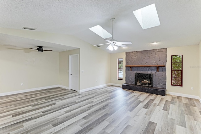 unfurnished living room featuring a textured ceiling, vaulted ceiling with skylight, a fireplace, light hardwood / wood-style floors, and ceiling fan