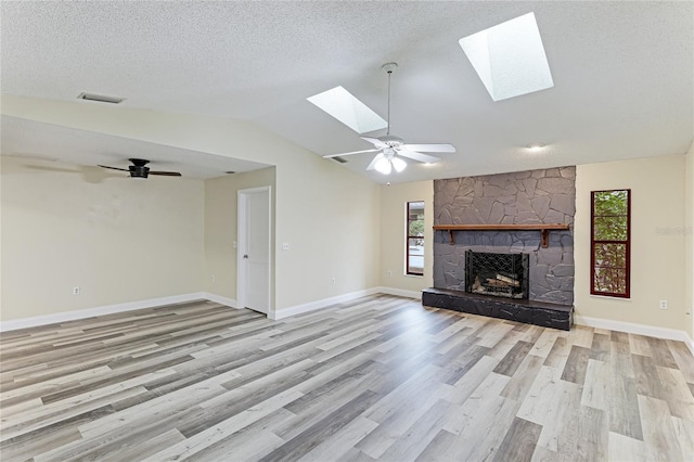 unfurnished living room featuring lofted ceiling with skylight, plenty of natural light, a fireplace, and a ceiling fan