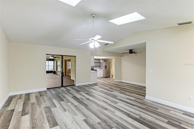 unfurnished living room with visible vents, baseboards, ceiling fan, vaulted ceiling with skylight, and light wood-style floors