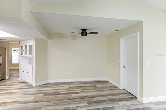 unfurnished room with visible vents, a textured ceiling, light wood-type flooring, and baseboards