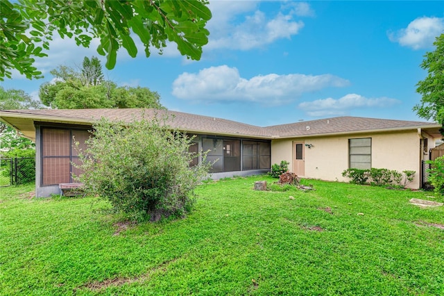 rear view of property featuring stucco siding, a lawn, fence, and a sunroom