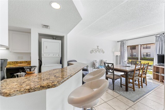 kitchen with white cabinets, stacked washer and dryer, light stone counters, a textured ceiling, and light tile patterned floors