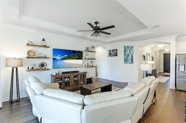 living room with ceiling fan, wood-type flooring, a tray ceiling, and ornamental molding