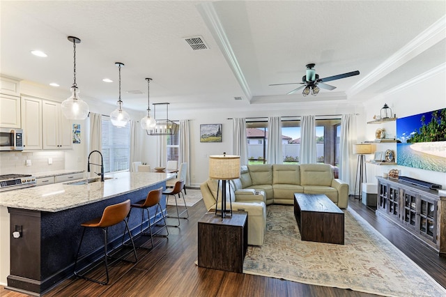 living room with crown molding, a tray ceiling, ceiling fan, sink, and dark wood-type flooring