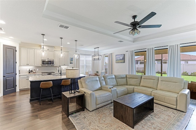 living room with ceiling fan, a raised ceiling, sink, and light hardwood / wood-style floors