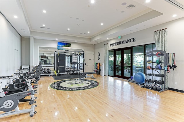 gym featuring french doors, a raised ceiling, and light wood-type flooring