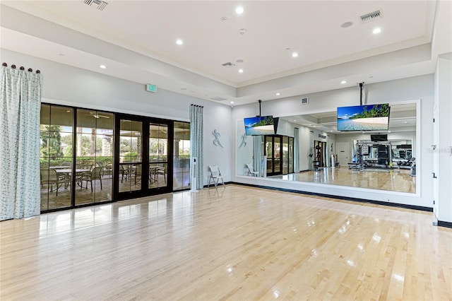 exercise room featuring a tray ceiling, light hardwood / wood-style flooring, and french doors