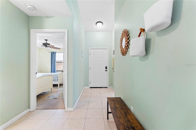 corridor with a textured ceiling, baseboards, and light tile patterned floors