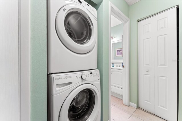 laundry area with sink, light tile patterned flooring, and stacked washer / dryer