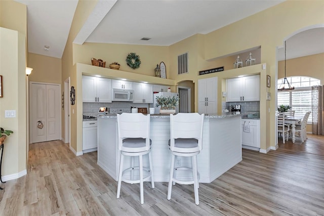 kitchen with decorative backsplash, light hardwood / wood-style flooring, a kitchen island, white cabinetry, and white appliances