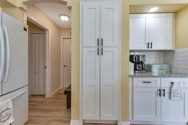 kitchen featuring decorative backsplash, light wood-type flooring, light stone countertops, white cabinets, and white fridge