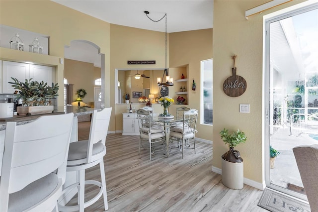 dining room featuring ceiling fan, high vaulted ceiling, light hardwood / wood-style flooring, and built in features