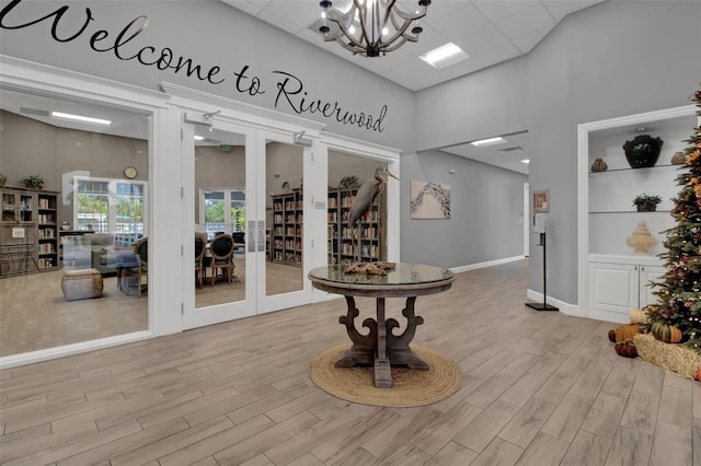 interior space featuring a high ceiling, a notable chandelier, french doors, and light wood-type flooring