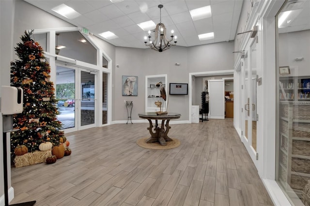 corridor featuring an inviting chandelier, french doors, a high ceiling, light wood-type flooring, and a drop ceiling