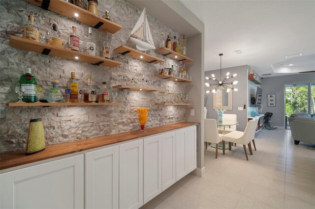 bar with hanging light fixtures, butcher block counters, white cabinets, an inviting chandelier, and light tile patterned floors