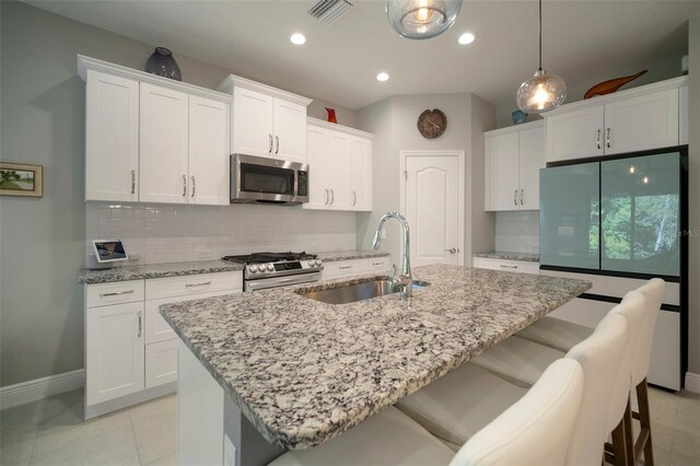 kitchen with stainless steel appliances, white cabinets, an island with sink, sink, and backsplash