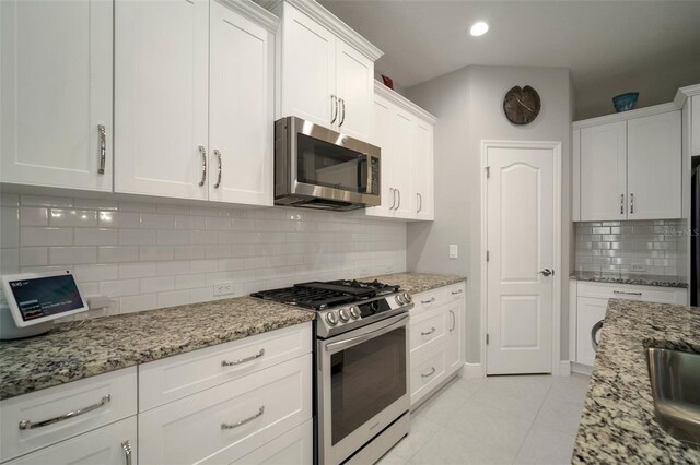 kitchen with stainless steel appliances, white cabinets, light tile patterned floors, decorative backsplash, and light stone countertops