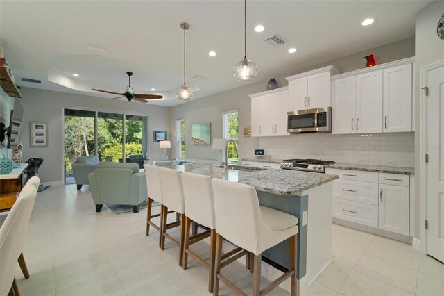 kitchen featuring white cabinetry, tasteful backsplash, light stone counters, a tray ceiling, and stove