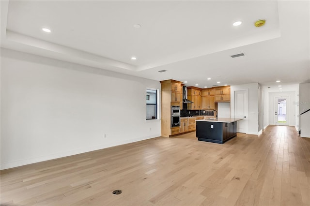 kitchen with a kitchen island with sink, light hardwood / wood-style flooring, a tray ceiling, stainless steel double oven, and a breakfast bar area