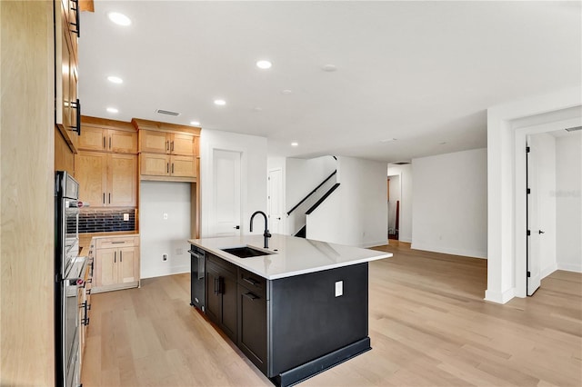 kitchen featuring backsplash, light hardwood / wood-style flooring, a kitchen island with sink, and sink