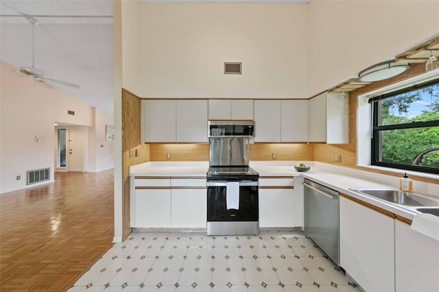 kitchen featuring white cabinetry, a textured ceiling, light parquet floors, stainless steel appliances, and high vaulted ceiling