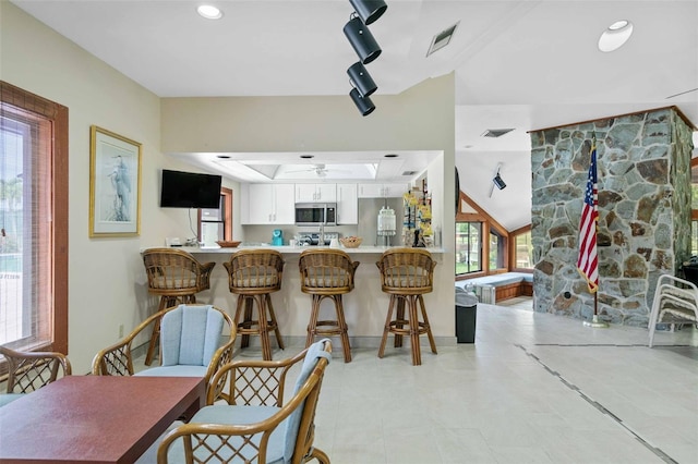 kitchen with light tile patterned floors, ceiling fan, white cabinets, vaulted ceiling, and kitchen peninsula