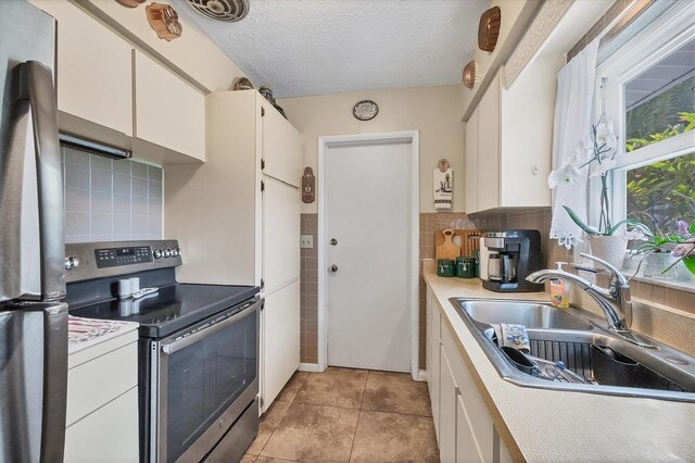 kitchen featuring light tile patterned floors, white cabinets, backsplash, appliances with stainless steel finishes, and sink