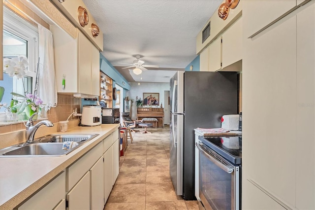 kitchen featuring sink, light tile patterned floors, stainless steel electric range oven, a textured ceiling, and ceiling fan