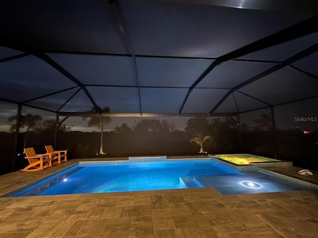 pool at twilight featuring an in ground hot tub, glass enclosure, and a patio area